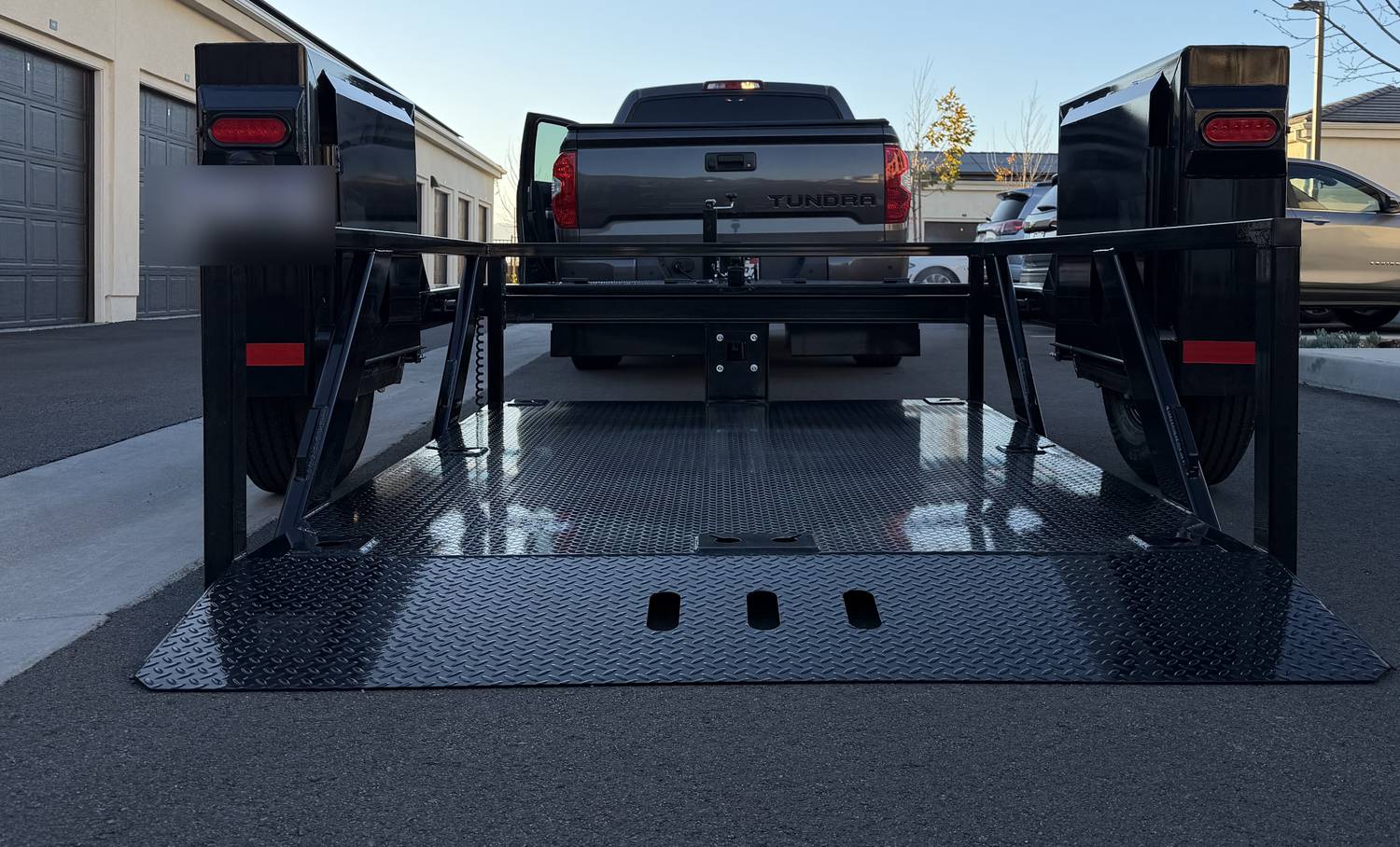 Single axle drop deck trailer with the deck lowered flat onto the pavement behind a pickup truck